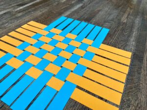 Geweven patroon van blauwe en gele stroken op houten tafel als visualisatie van verbinding en samenwerking