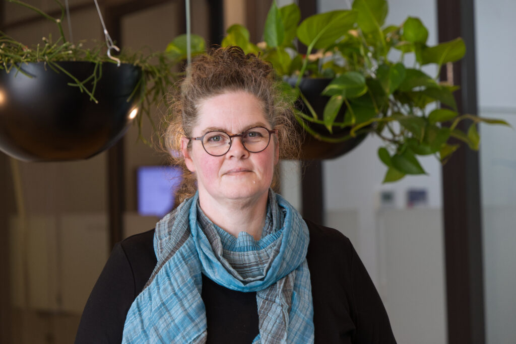Portret van Renate Postma met bril en sjaal, binnen gefotografeerd bij planten