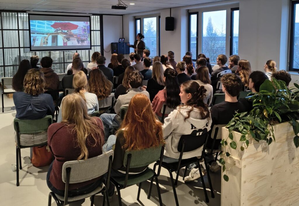 Presentatie in zaal met studenten die luisteren naar spreker bij projectbijeenkomst