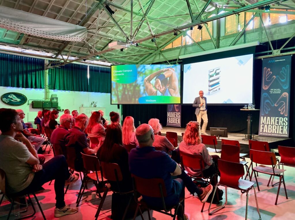 Presentatie tijdens bijeenkomst in Makersfabriek met spreker op podium en publiek in zaal