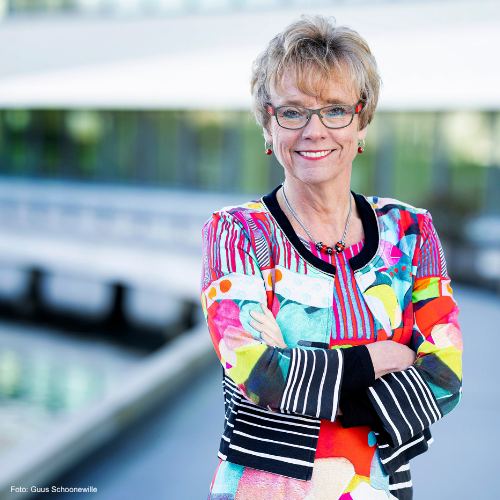 Portretfoto van Annemieke Nijhof met bril en kleurrijke kleding, buiten gefotografeerd bij modern gebouw