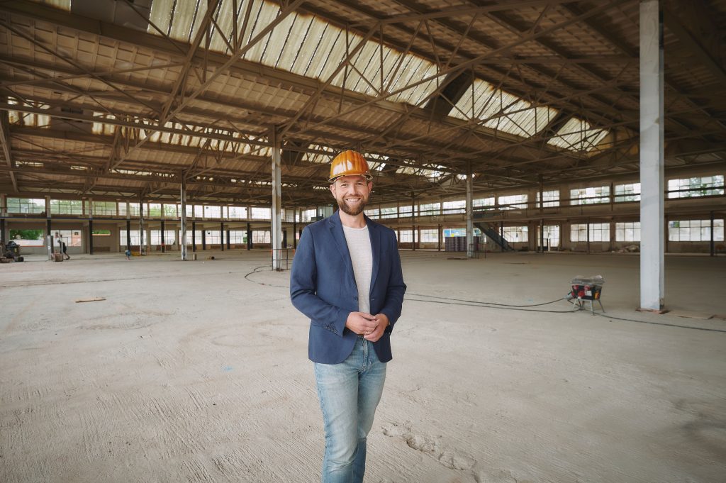 Rene Bremen staat lachend in een grote, nog lege industriële hal op het terrein van de Makersfabriek in Zwolle met een bouwhelm op